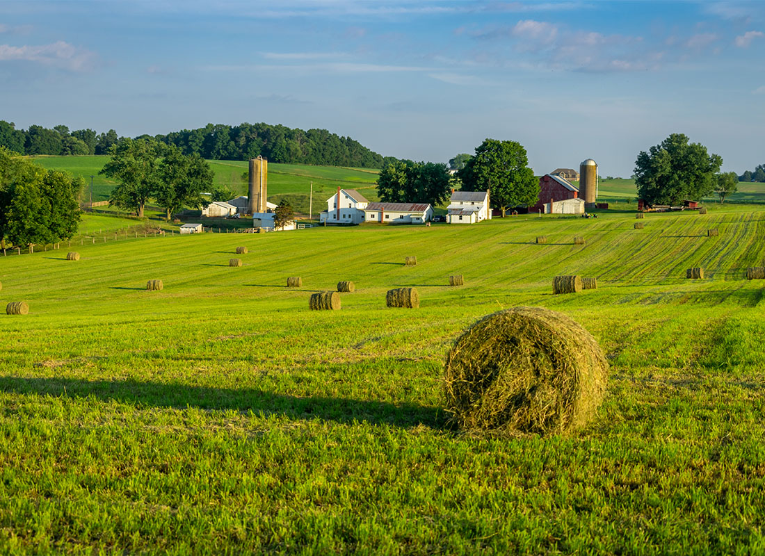 About Our Agency - Round Hay Bales on Slightly Rolling Hills in Amish Country With a Farm House in the Background